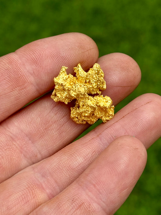 gold nugget held in a hand against a green background