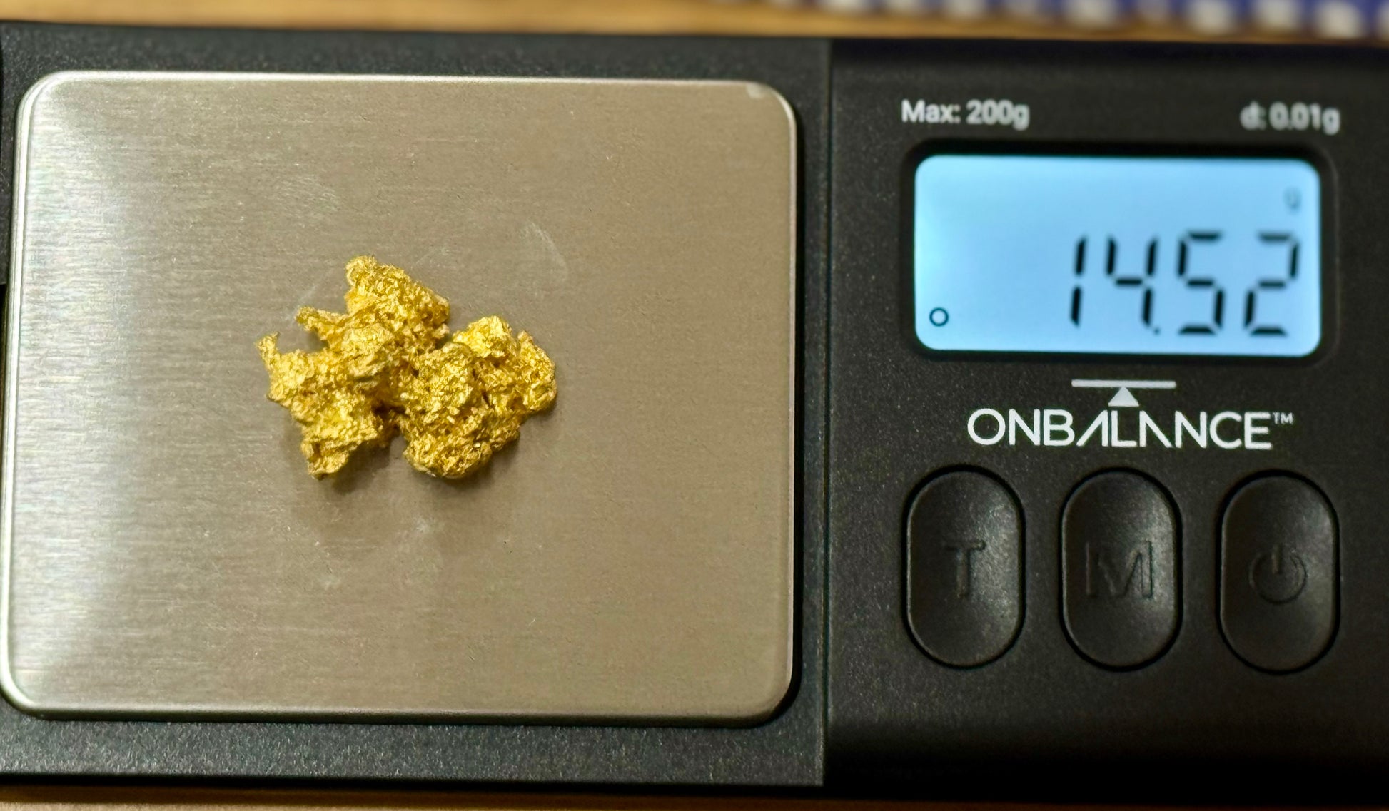 Gold nuggets on a digital scale with a displayed weight, branded 'On Balance'.
